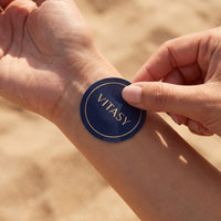 Fingers pressing a Vitasy patch onto the wrist