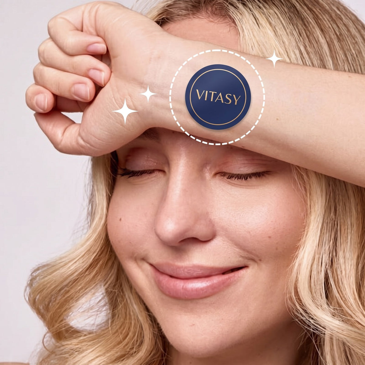 Smiling woman resting her wrist on her forehead, wearing a navy Vitasy patch