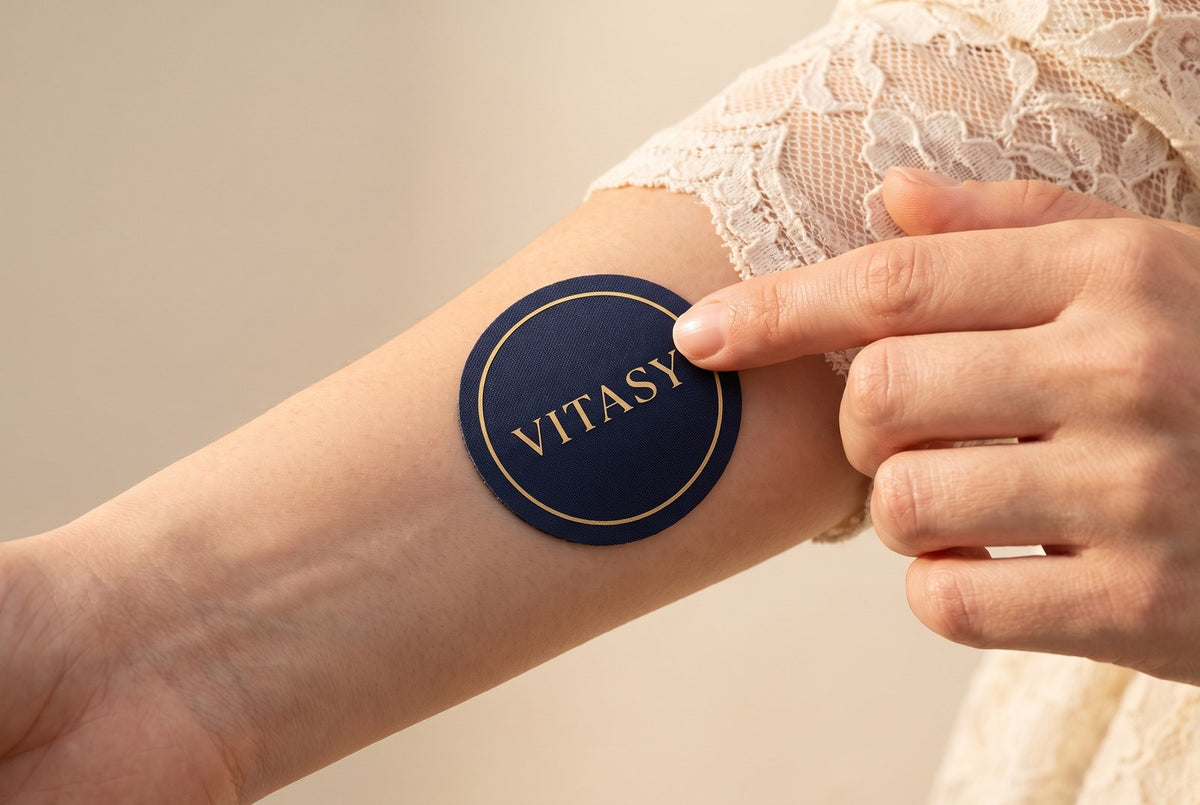 Hand applying a navy Vitasy patch to a forearm