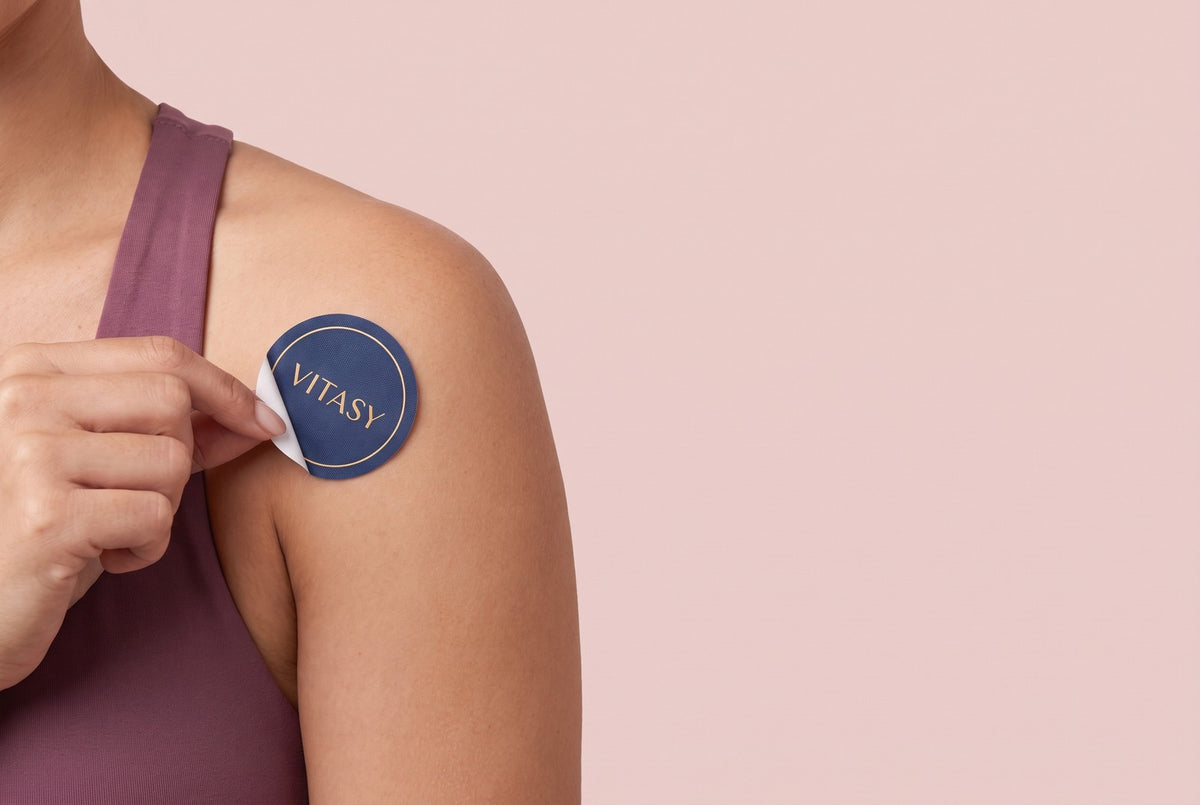 Woman applying a navy Vitasy patch to her shoulder