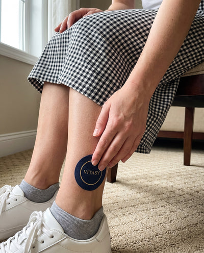 Pressing a round navy Vitasy patch onto the ankle