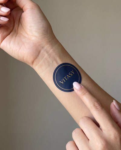 Pressing a round navy Vitasy patch onto the forearm