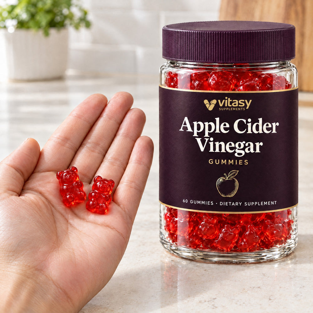 An adult hand holding two red gummy bears next to the Vitasy jar on a kitchen counter