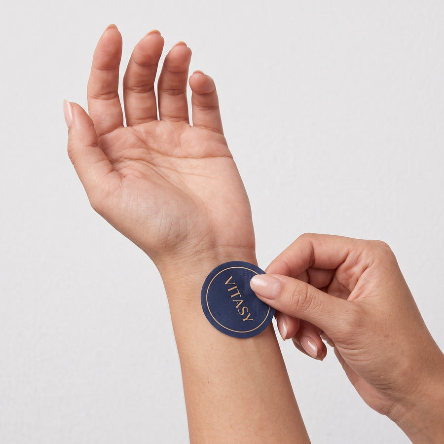 Fingers pressing a Vitasy patch onto the inner wrist