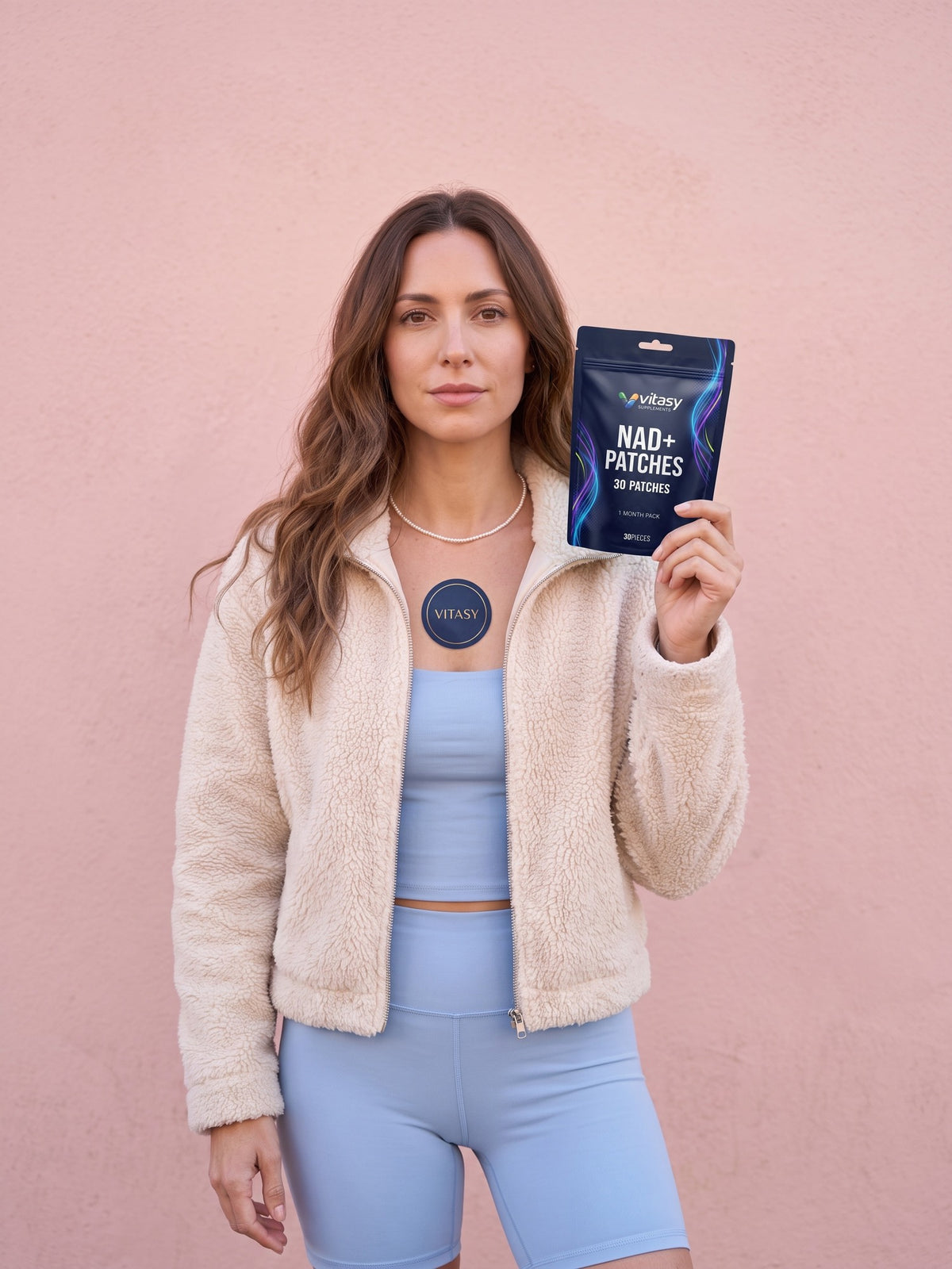 Woman wearing a navy Vitasy NAD+ patch on her upper chest and holding the pouch
