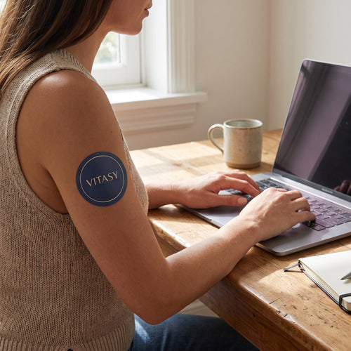Vitasy patch on an upper arm while working at a laptop