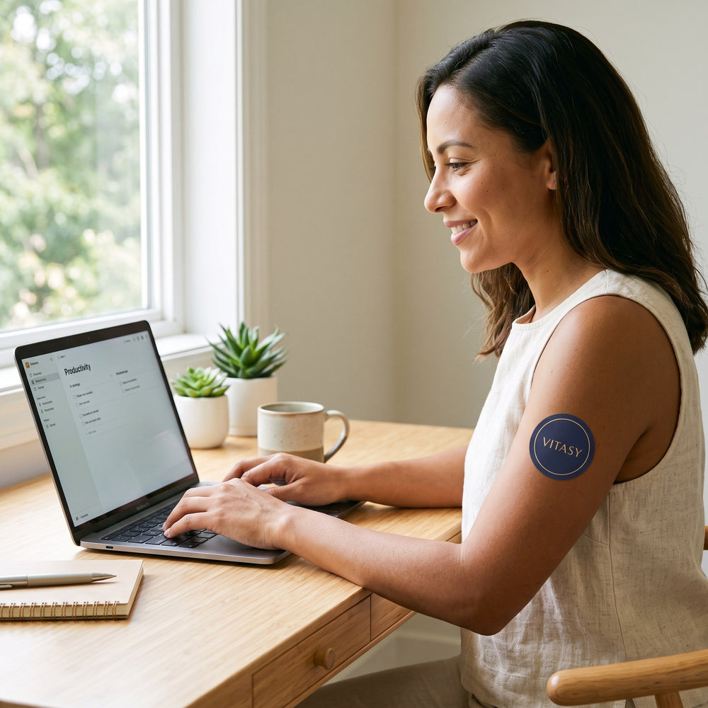 Woman working at a desk with a Vitasy patch on her upper arm