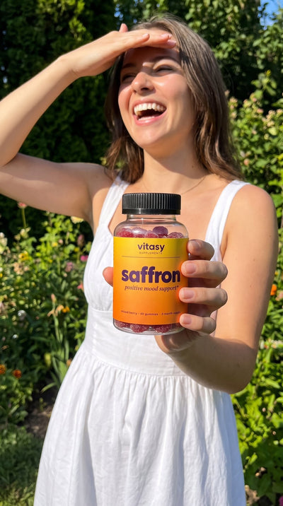 Woman in a sunny garden holding Vitasy Saffron Gummies