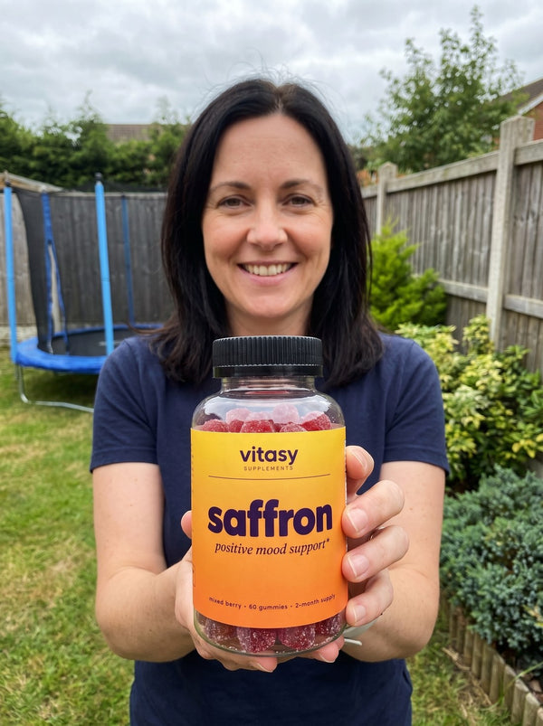 Mom holding a bottle of Vitasy Saffron Gummies in the backyard