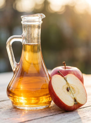 Apple cider vinegar in a glass carafe with a red apple