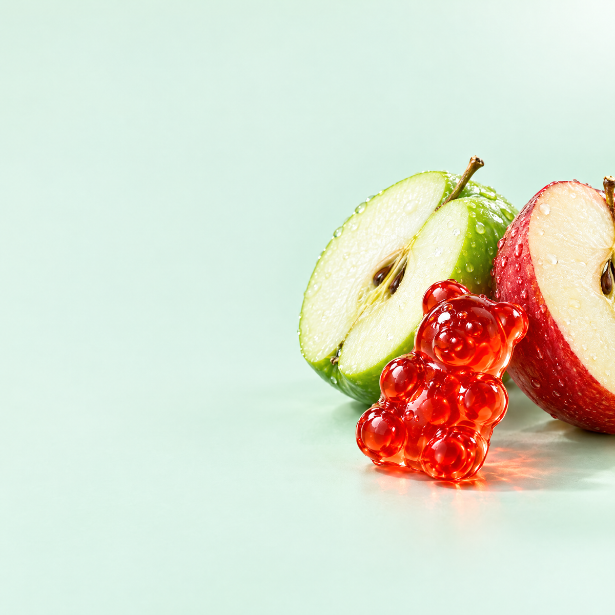Red apple cider vinegar gummy bear in front of halved apples