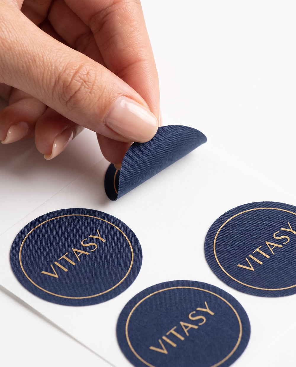 Fingers peeling a round navy Vitasy patch from its backing sheet