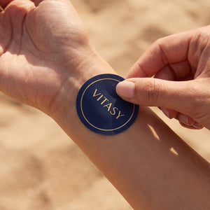 Fingers pressing a Vitasy patch onto the wrist
