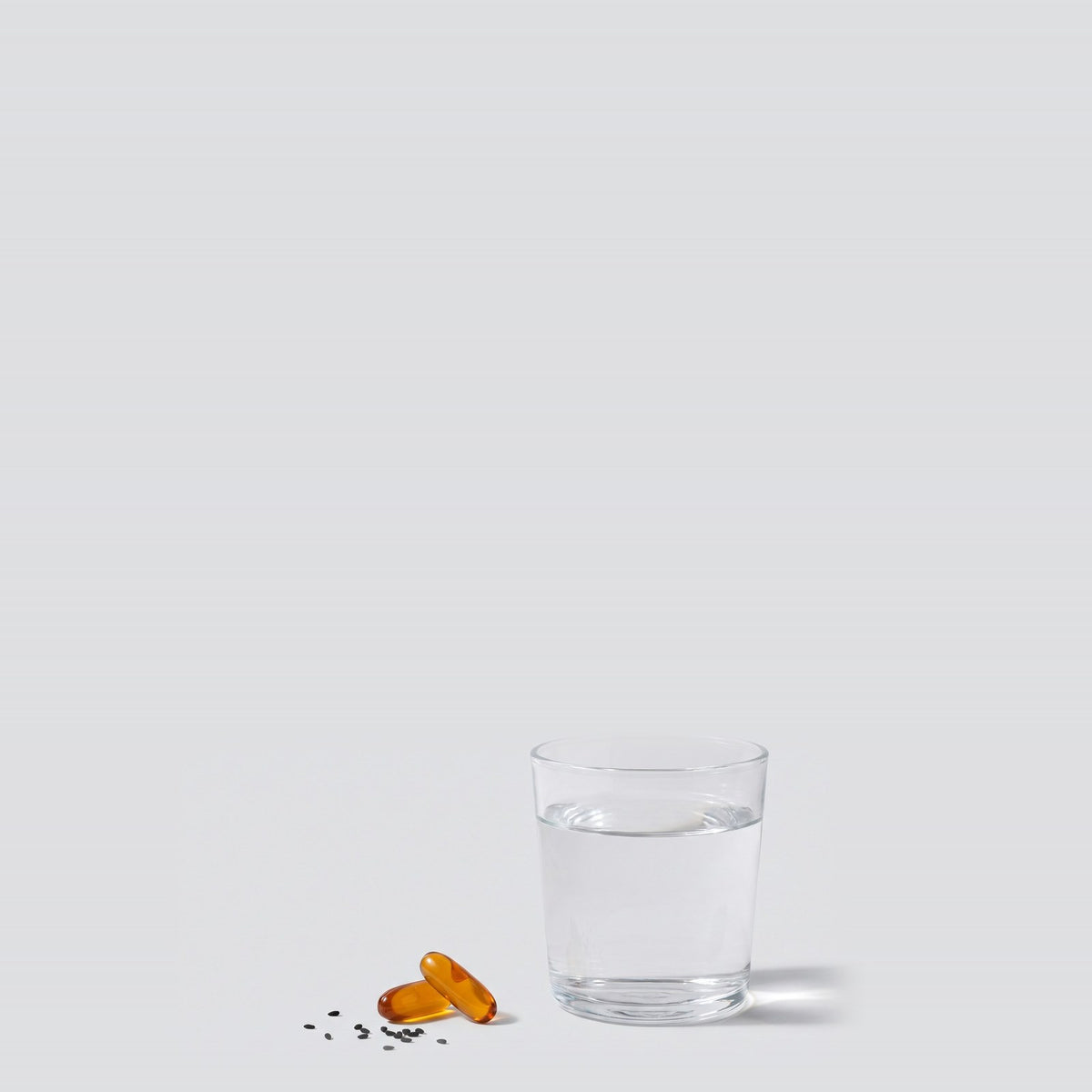 Two black seed softgels next to a glass of water