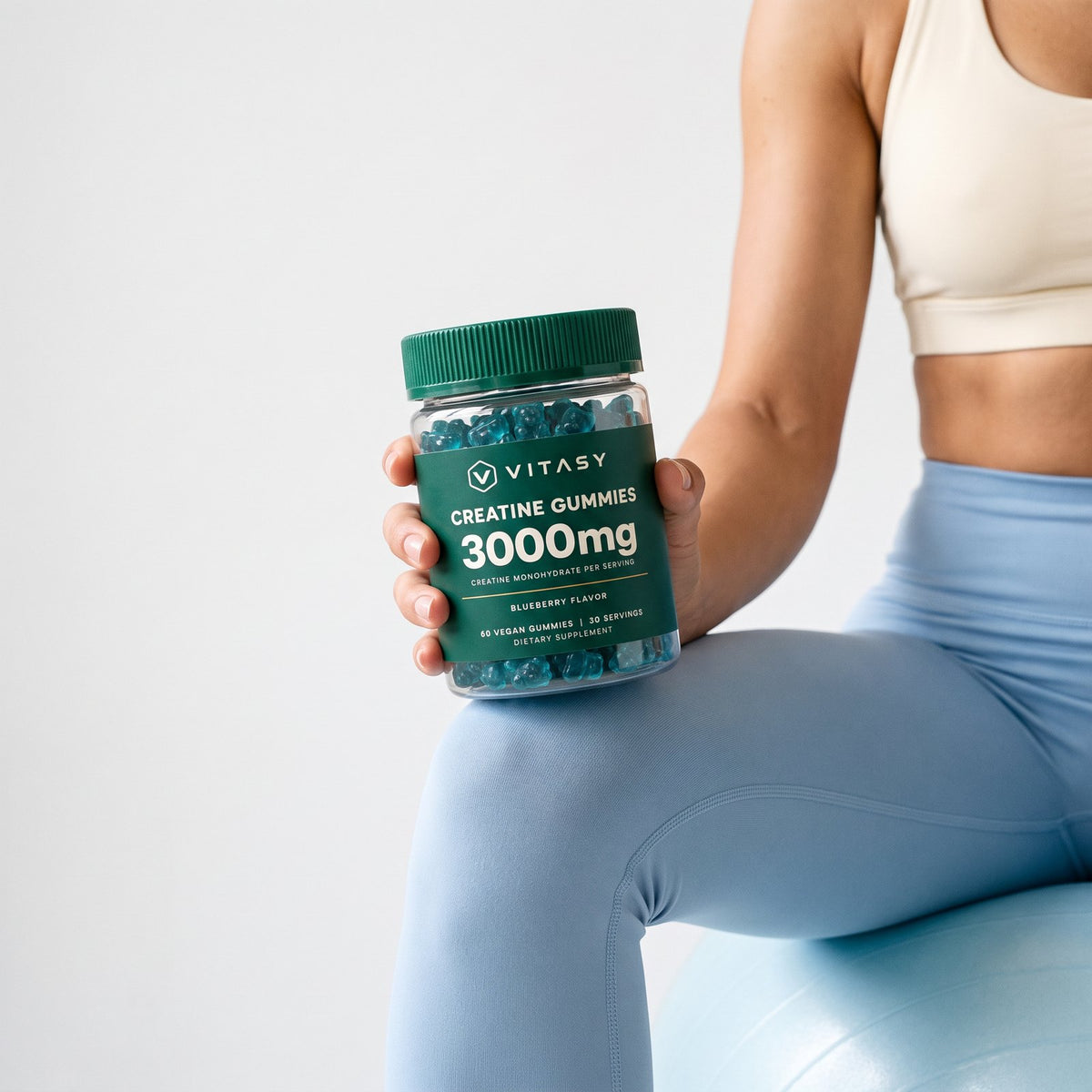 Woman on an exercise ball holding a jar of Vitasy Creatine Gummies