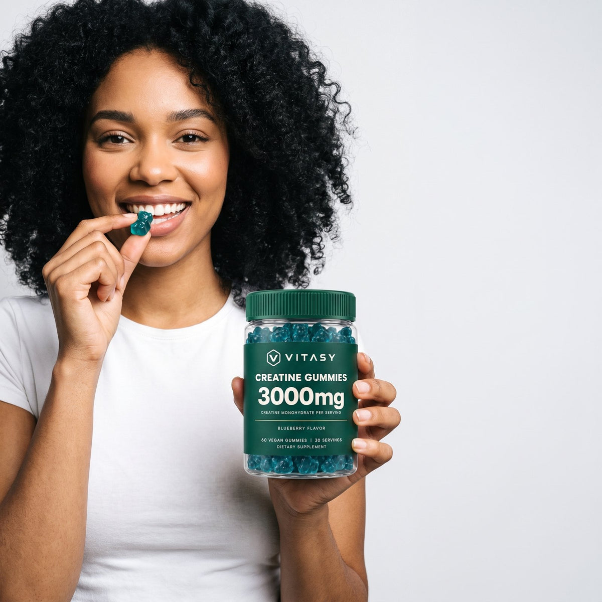 Woman holding a jar of Vitasy Creatine Gummies and eating a gummy