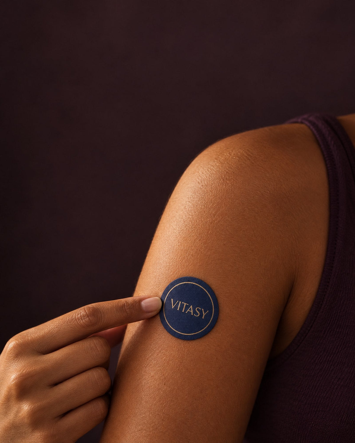 Fingertip pressing a Vitasy energy patch onto the upper arm