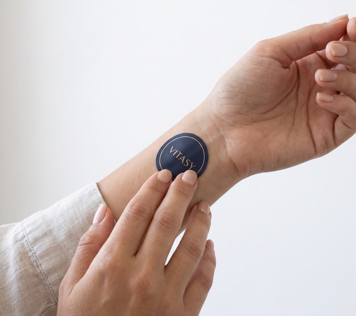 Hands applying a navy Vitasy patch to the inner wrist