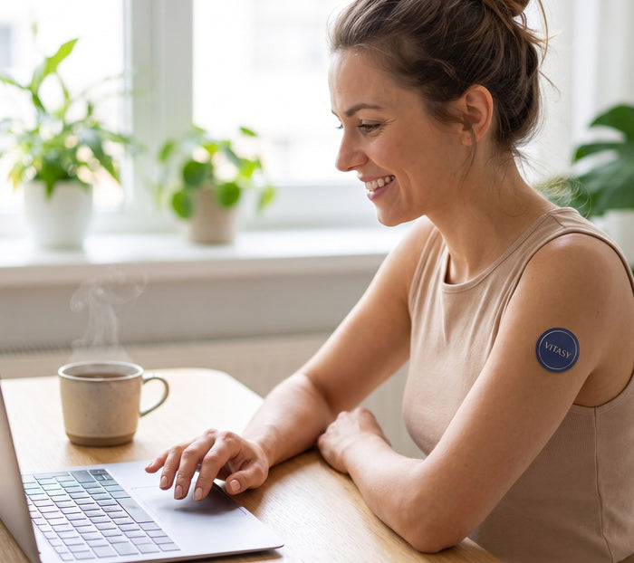 Smiling woman at her desk with a Vitasy patch on her upper arm