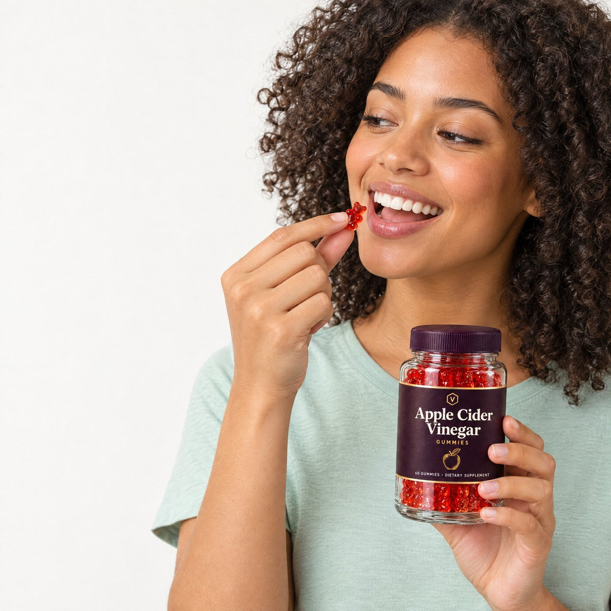 Woman eating a red gummy and holding a jar of Vitasy Apple Cider Vinegar Gummies