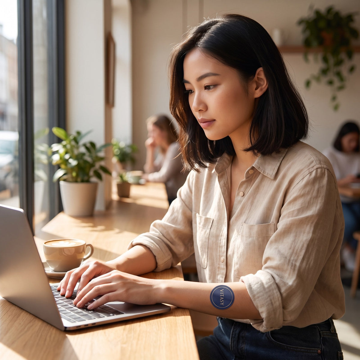 Woman working on a laptop in a cafe wearing a Vitasy patch