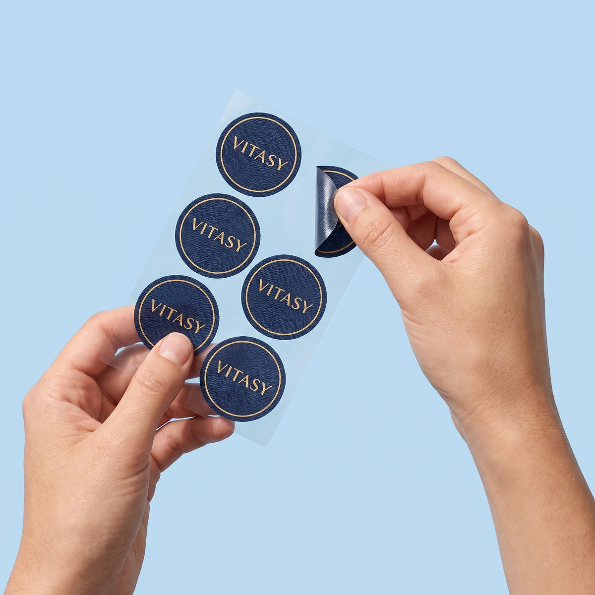 Peeling a round navy Vitasy patch from its sheet and applying it to the wrist