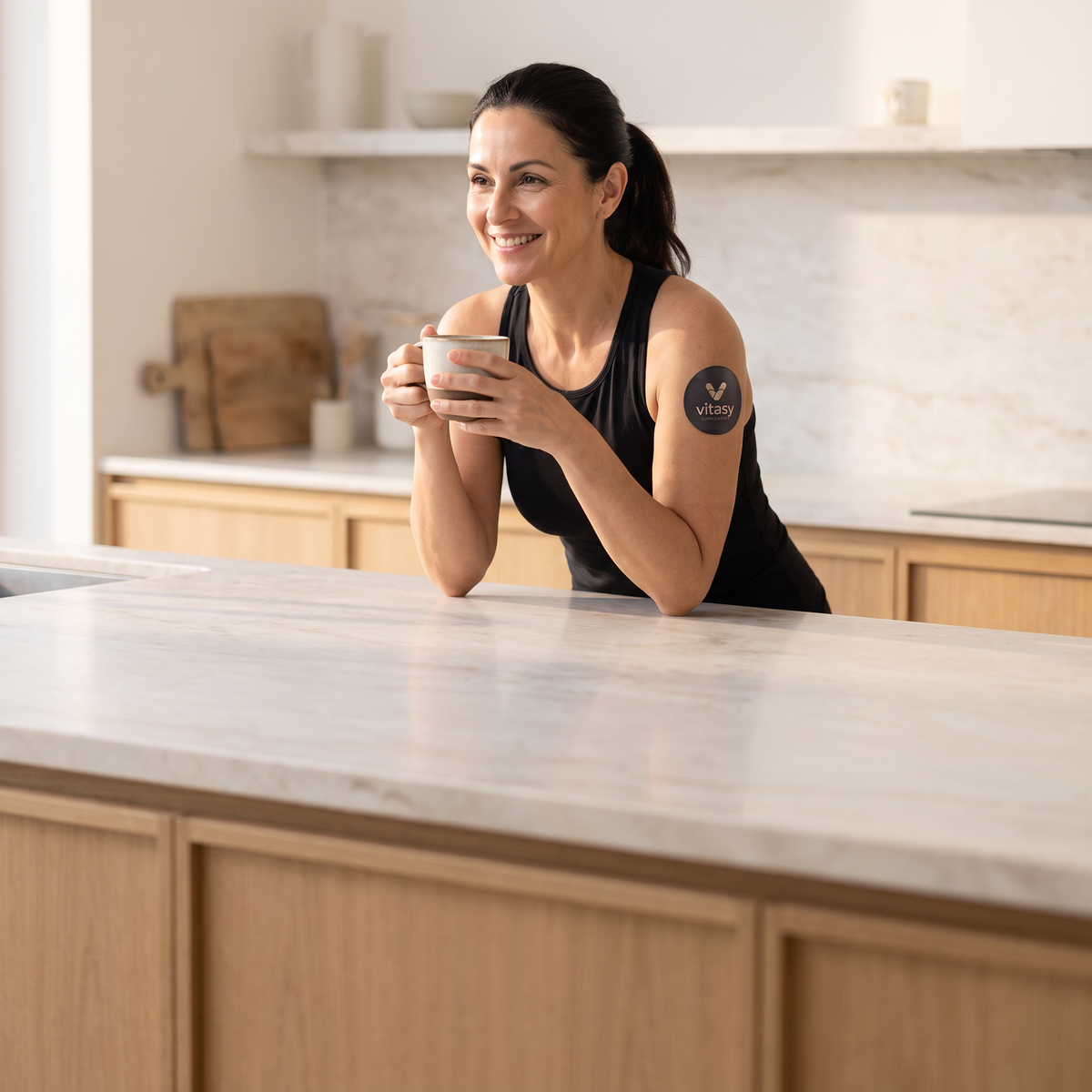 Woman with a Vitasy patch on her upper arm holding a coffee cup in the kitchen