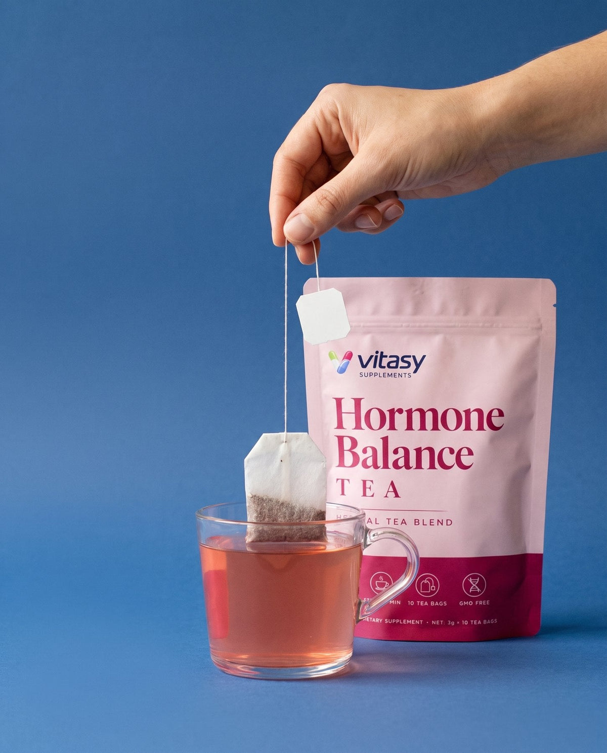 Tea bag being dipped into a cup of herbal tea next to the Vitasy pouch