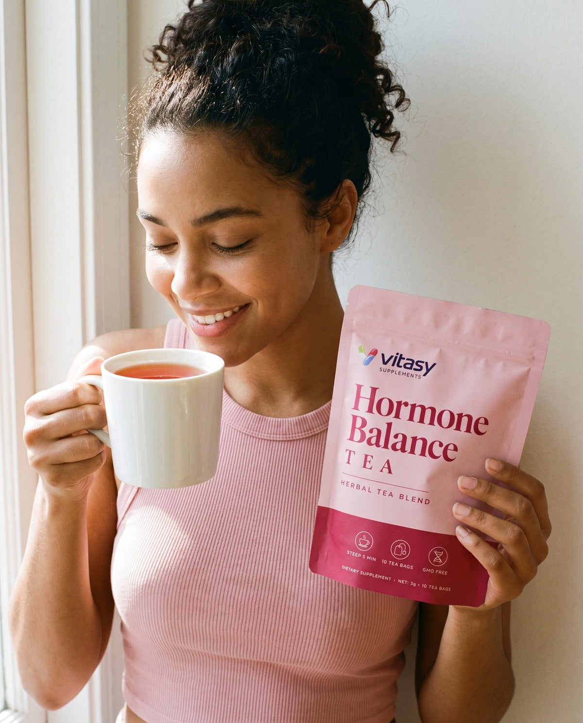 Woman enjoying a cup of Vitasy herbal tea and holding the pouch