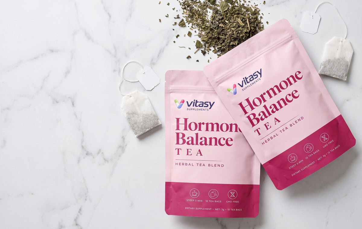 Two Vitasy herbal tea pouches on white marble with tea bags and dried herbs