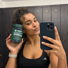 Woman taking a mirror selfie in a gym locker room with a jar of Vitasy Creatine Gummies