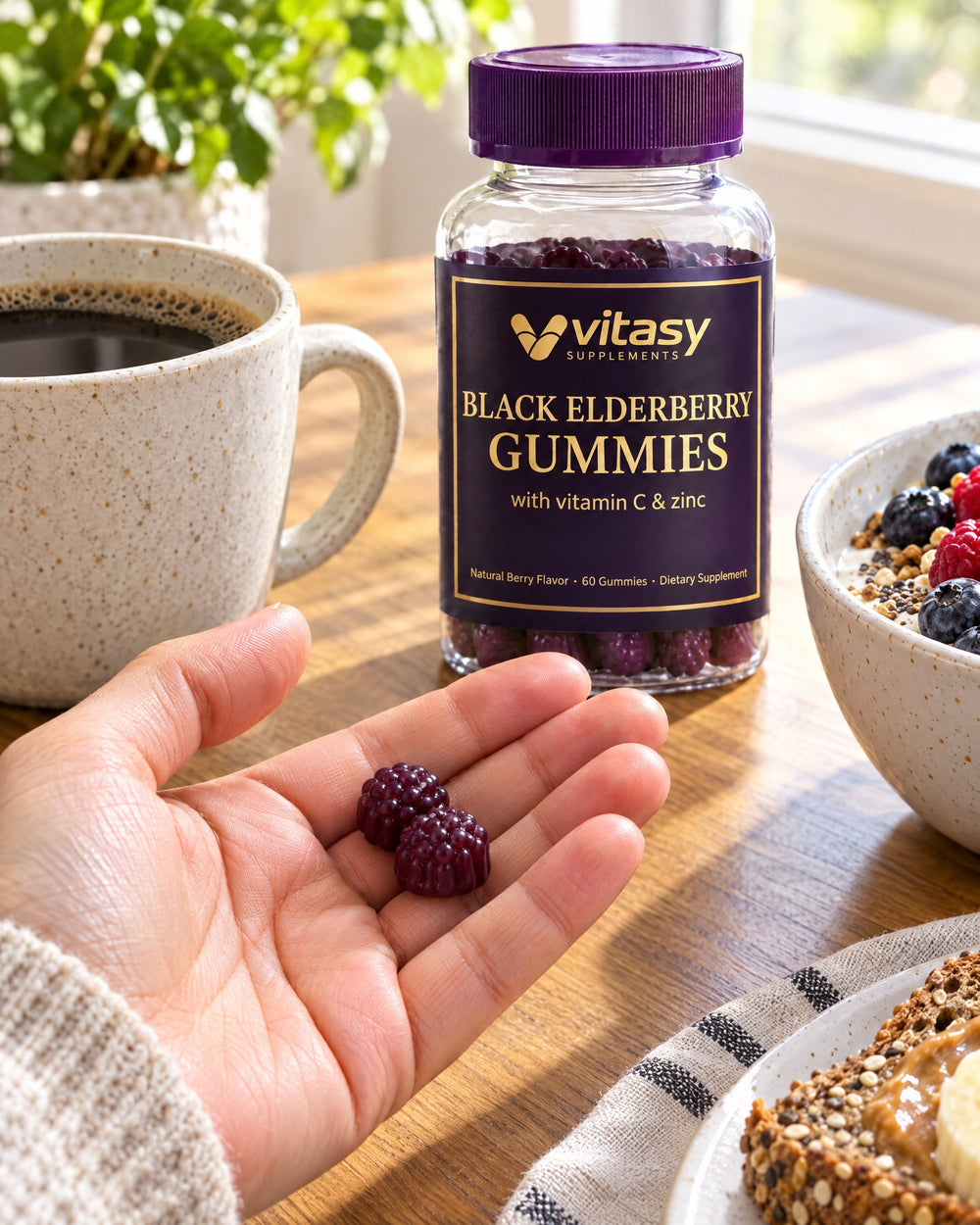 Hand holding two dark purple elderberry gummies at breakfast next to the Vitasy jar