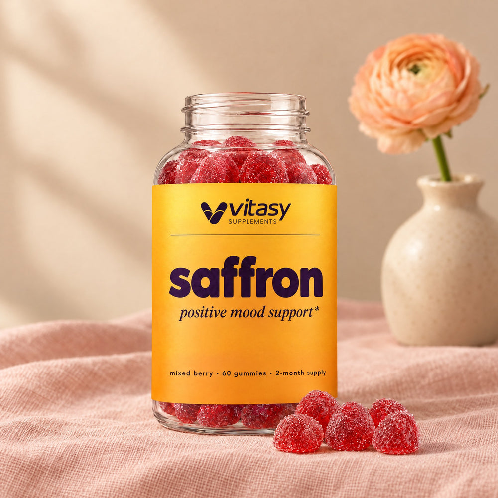 Vitasy Saffron Gummies bottle on blush linen next to a peach flower in a vase