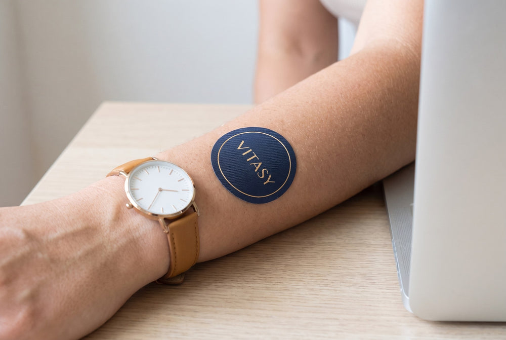 Forearm with a Vitasy patch next to a wristwatch