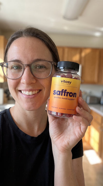 Woman holding a bottle of Vitasy Saffron Gummies in her kitchen