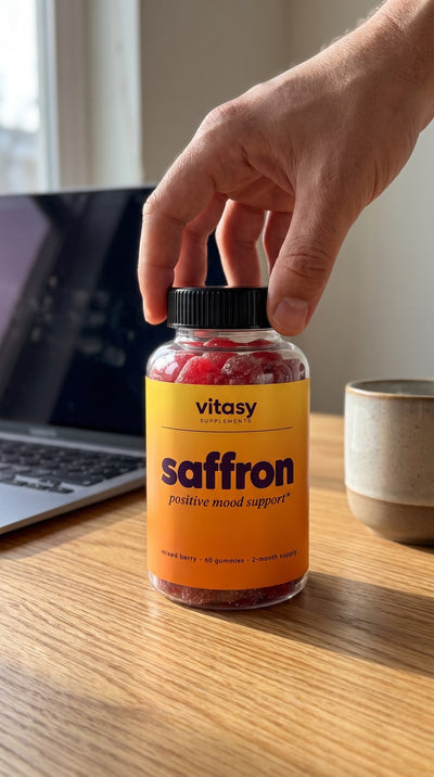 Bottle of Vitasy Saffron Gummies on a desk next to a laptop