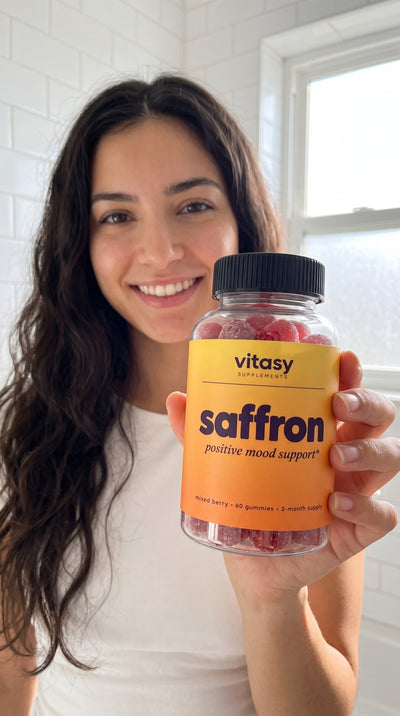 Woman holding Vitasy Saffron Gummies in a bright bathroom