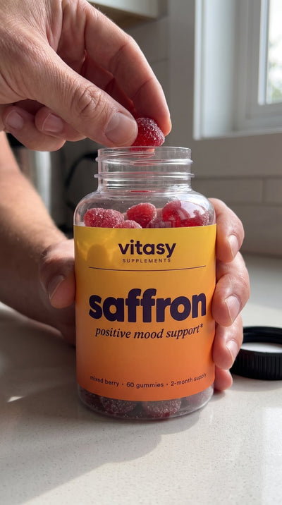Hand taking a mixed berry gummy from an open bottle