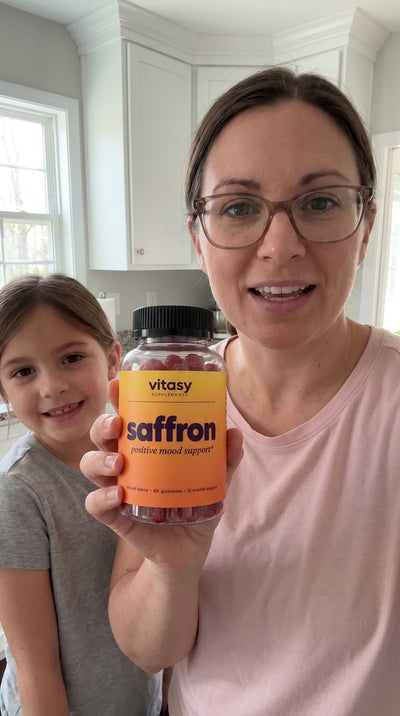 Parent holding a jar of Vitasy Saffron Gummies in a bright kitchen with a child nearby