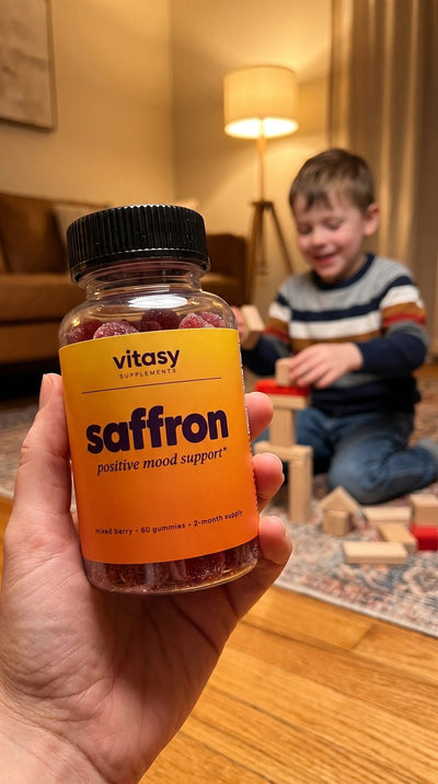 Parent holding Vitasy Saffron Gummies in a cozy living room while a child plays