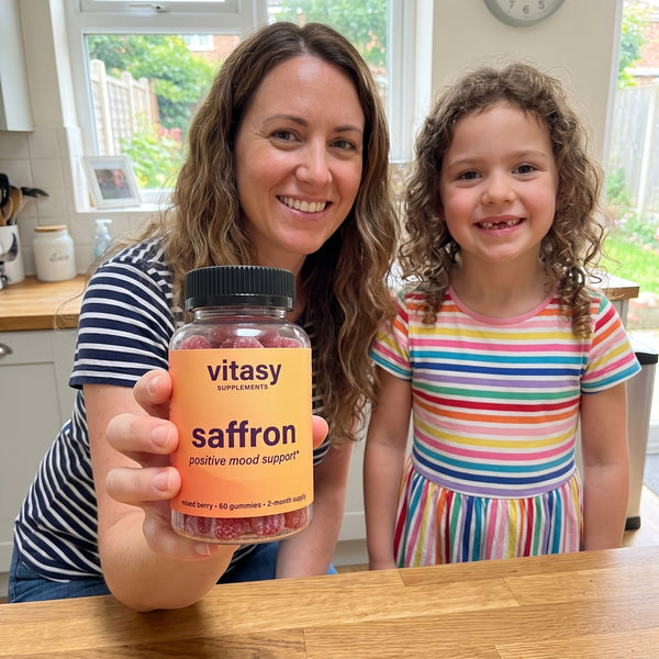 Mom holding a bottle of Vitasy Saffron Gummies next to her smiling daughter in the kitchen